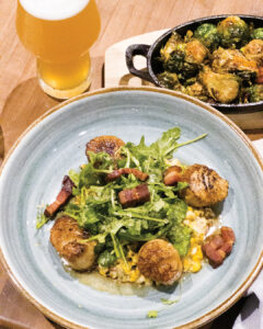 Chef Chat: Lyle Broussard - Louisiana Cookin' Chef Lyle Broussard lets us in on the secret to success. Blue bowl with seared scallops, greens, and bacon over grains, topped with arugula; beer glass to the left and a skillet of vegetables in the background.