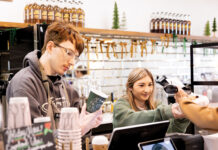 How STIR Coffee House Is Brewing Community in Baton Rouge Two baristas at a coffee shop counter assist a customer; one holds a green cup while the other hands over sunglasses and a pastry.