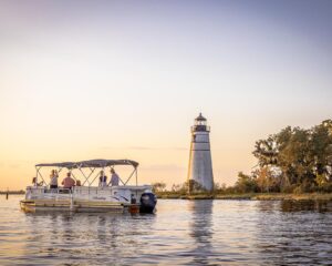 Worth the Drive: Small Towns with Big Charm - Louisiana Cookin'  Group of people on a canopy-covered boat cruising near a white lighthouse at sunset.