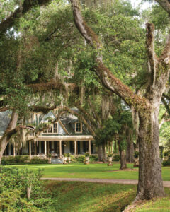 Worth the Drive: Small Towns with Big Charm - Louisiana Cookin'  Large house with a wraparound porch set on a grass lawn, framed by moss-draped oak trees in a lush yard.