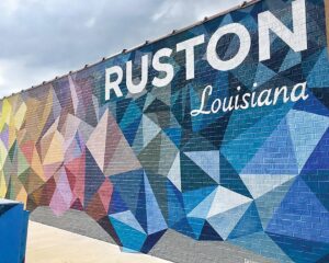 Worth the Drive: Small Towns with Big Charm - Louisiana Cookin'  Vibrant geometric mural on a brick wall that reads 'RUSTON Louisiana' with bold, white lettering and a multicolor triangle pattern.