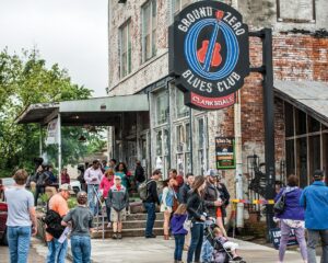 Weekend Away: Clarksdale, Mississippi - Louisiana Cookin' Set your sights on the Mississippi Delta for a soulful few days. Exterior view of Ground Zero Blues Club with a large circular sign reading 'Ground Zero Blues Club' and a crowd of people waiting outside on a brick building.