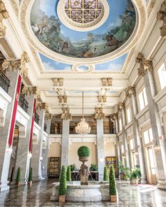 Worth the Drive: Small Towns with Big Charm - Louisiana Cookin'  Opulent hotel lobby with a domed painted ceiling, chandeliers, marble columns, and a central fountain surrounded by topiary.