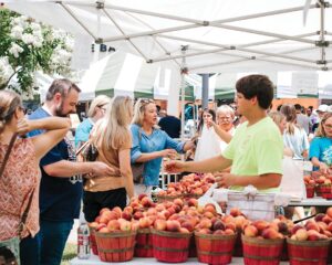 Worth the Drive: Small Towns with Big Charm - Louisiana Cookin'  People shop at an outdoor market, selecting red apples from baskets under white canopied stalls.