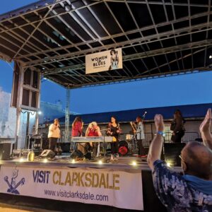 Weekend Away: Clarksdale, Mississippi - Louisiana Cookin' Set your sights on the Mississippi Delta for a soulful few days. A live band performs on an outdoor stage with a banner reading 'Visit Clarksdale' in front, audience members raise their hands nearby.