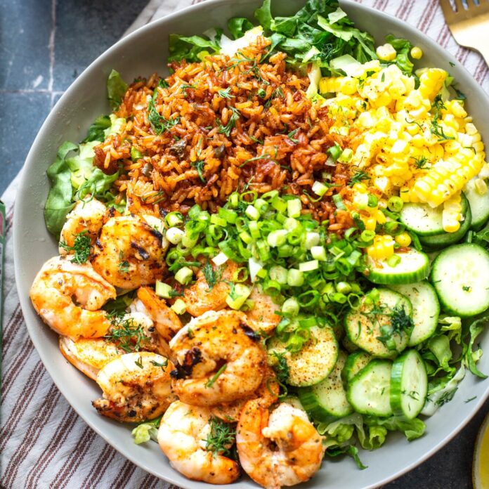 Shrimp and greens salad with corn, cucumber, scallions, and cilantro on a bowl of mixed greens and rice.