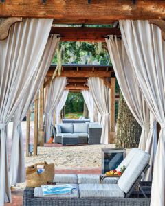 AK_PTLAK_Cabanas-Couple2 - Louisiana Cookin' Weekend Away: Press Pause in Fairhope, Alabama - Louisiana Cookin' A gentle weekend escape to a city full of coastal charm. Row of wooden cabanas with white curtains and gray wicker lounge furniture on a sandy beach.