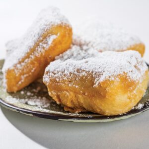 Beignets2_Rey-Lopez-2 - Louisiana Cookin' Making Waves: Louisiana’s Own Culinary Trailblazers - Louisiana Cookin' Louisiana-born chefs making their mark across the South. Powdered-sugar dusted fried dough pastries on a green plate.