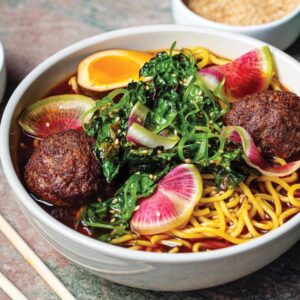 Brisket-Yakamein - Louisiana Cookin' Making Waves: Louisiana’s Own Culinary Trailblazers - Louisiana Cookin' Louisiana-born chefs making their mark across the South. Ramen bowl with glossy broth, crispy meatballs, soft-boiled egg, greens, and pink radish slices sprinkled with sesame seeds.