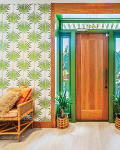 Entry_NeutralGround - Louisiana Cookin' Making Waves: Louisiana’s Own Culinary Trailblazers - Louisiana Cookin' Louisiana-born chefs making their mark across the South. Wooden door with green trim in a tropical-themed entry, palm-patterned wallpaper and a wicker chair with orange cushions nearby.