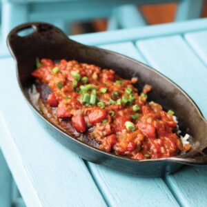 IMG_5369 - Louisiana Cookin' Making Waves: Louisiana’s Own Culinary Trailblazers - Louisiana Cookin' Louisiana-born chefs making their mark across the South. Cast-iron skillet with a tomato-based sauce over rice, topped with chopped green onions, on a turquoise table.