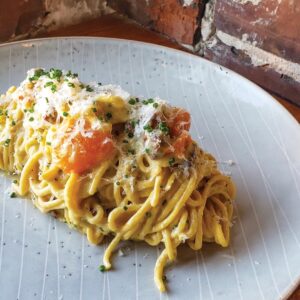 NG-Carbonara - Louisiana Cookin' Making Waves: Louisiana’s Own Culinary Trailblazers - Louisiana Cookin' Louisiana-born chefs making their mark across the South. Creamy fettuccine with salmon chunks, grated cheese, and chives on a white plate.