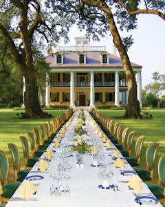 Unknown - Louisiana Cookin' Putting His Heart on the Plate: Inside Chef Jeremy Langlois’ Culinary Journey - Louisiana Cookin' Chef Jeremy Langlois reflects on his decades-long culinary journey—from training under legendary John Folse to Houma's House to his latest venture, a self-published cookbook. Long outdoor banquet table set with napkins and glassware extends toward a white-columned mansion on a green lawn, framed by large trees.