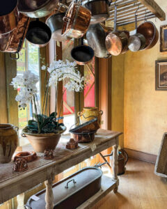 Unknown-5 - Louisiana Cookin' Weekend Away: Press Pause in Fairhope, Alabama - Louisiana Cookin' A gentle weekend escape to a city full of coastal charm. Ceiling with copper pots hanging above a rustic wooden table displaying ceramic pots and a potted orchid plant near a window.
