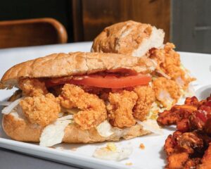 web-Gravy3CreditTrevorJohnsonMaraisStudios - Louisiana Cookin' New + Interesting: July/August 2026 - Louisiana Cookin' Catch up on all the latest happenings across the Bayou state, with must-try restaurants and so much more. Crispy fried chicken sandwich with tomato slices and shredded lettuce on a crusty bun, plated on a white dish.
